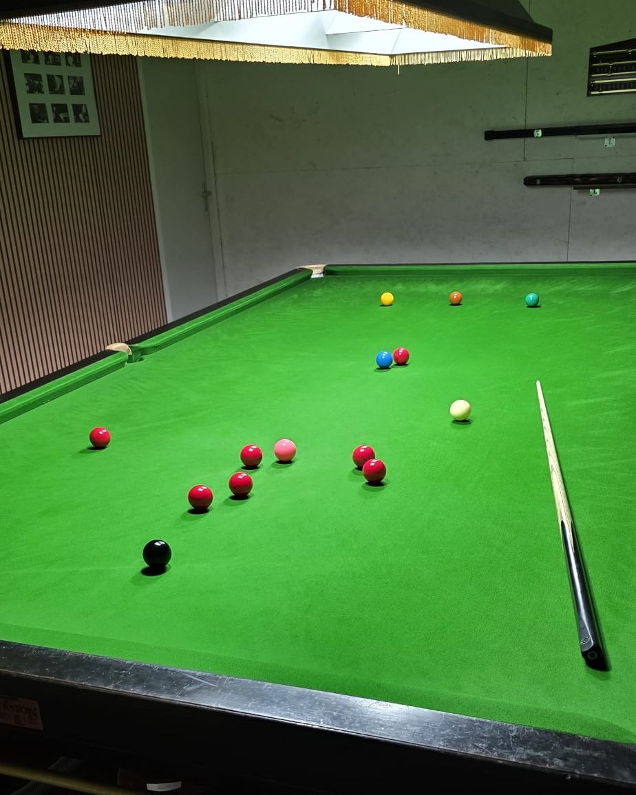 Onze snookertafel in de loods in IJmuiden, onder de lamp, met alle kleuren op hun spot en een paar rode eromheen